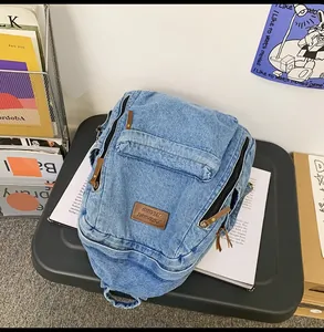 Detail view of light blue denim backpack with brown leather logo patch and multiple zippers