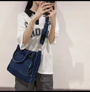 Detail of dark blue denim crossbody bag featuring a front pocket and wide adjustable strap