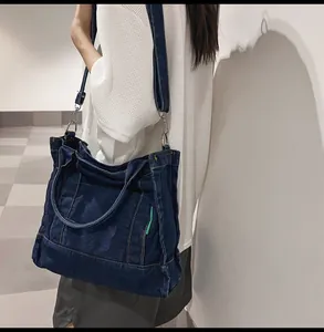 Detail view of large dark blue denim tote bag with metal hooks and green side label