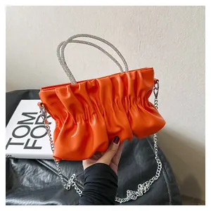 Detail of orange pleated cloud bag with shimmering rhinestone handles and silver chain