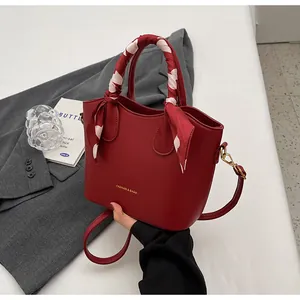 Détail d'un sac seau rouge en cuir avec poignée en foulard de soie et lettrage doré