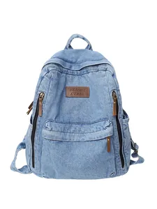 Large denim backpack for women featuring light blue washed fabric and brown leather label