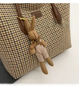 Detail of a brown knit bunny pendant with bow and plaid pants on a matching tote bag