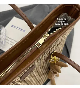 Detailed macro view of the smooth golden metal zipper on this brown plaid tote bag