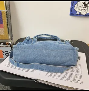 Detail of light blue washed denim bag with white stitching and metal strap rings