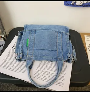 Detailed shot of a blue denim tote bag with green logo label on a black stand