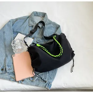 Detail of black nylon tote bag featuring neon green braided chain and drawstring sides