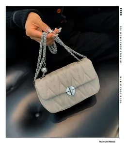 Détail d'un sac matelassé beige avec fermoir cylindrique argenté et bandoulière chaîne