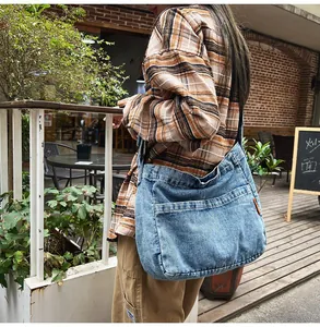 Detail of blue denim crossbody bag featuring large front pocket and orange side label