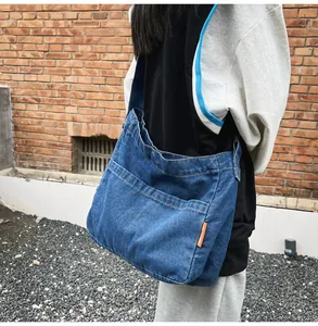 Detail of blue denim crossbody bag featuring a bright orange tag and washed texture
