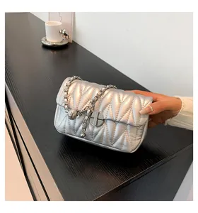 Détail du sac argenté matelassé avec finition métallique et fermoir rond sur bois