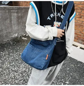 Detail view of durable navy blue denim crossbody bag featuring large front pocket and orange tag