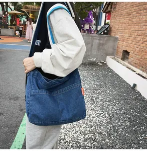 Detail of deep blue washed denim crossbody bag featuring dual front pockets and wide strap