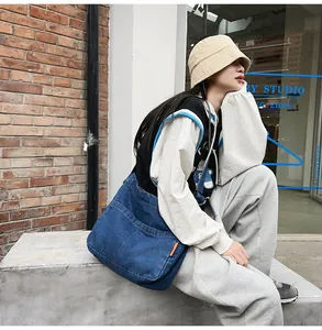 Outdoor lifestyle view of large dark blue denim crossbody bag with orange side label