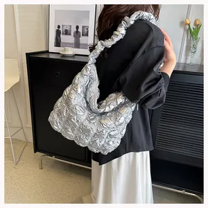 Detailed view of silver quilted puff shoulder bag with ruffled strap on a model