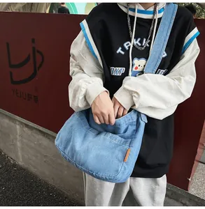Detail of light blue denim crossbody bag with front pocket and orange side label
