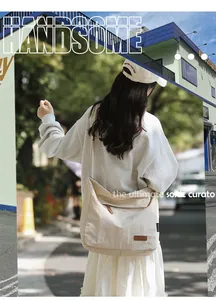 Detail of a beige canvas crossbody bag with brown leather logo patch in a street style view