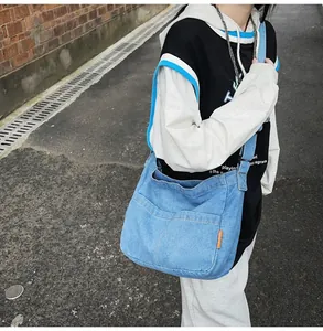 Detail of light blue washed denim crossbody bag with side pockets and orange label