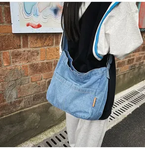 Close-up of light blue denim crossbody bag with side label against red brick wall