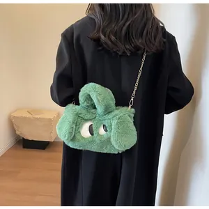 Borsa di peluche verde con occhi di cartone e catena d'oro indossata su cappotto