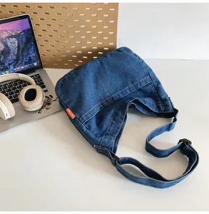 Detail of dark blue denim crossbody bag with orange label in a desktop setting