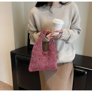 Detail of rose red woven tote bag with glitter finish held by a model in a cozy setting