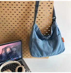 Detail of blue denim crescent bag with orange label and adjustable strap in campus setting