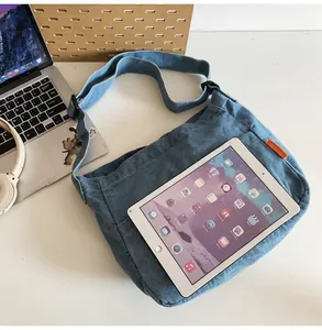Close-up of light blue denim crossbody bag featuring an adjustable strap and orange label