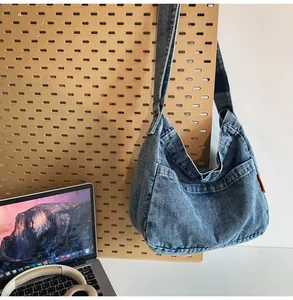 Detail of blue denim crescent crossbody bag with orange tag on wooden pegboard