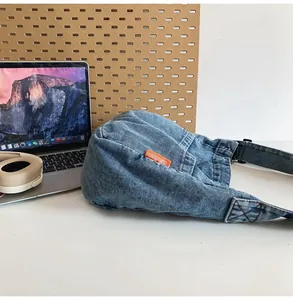 Detail of light blue denim crossbody bag with orange woven label on a desk with a laptop