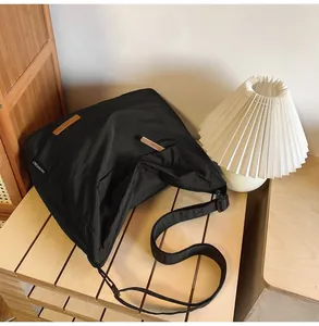 Detail of black canvas tote showing leather accents and adjustable strap on a wooden table