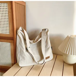 Close-up of beige canvas tote bag detail with brown leather logo patch on wood surface