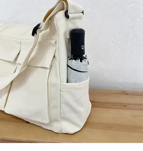 Dettaglio borsa a tracolla in tela beige con tasche anteriori e portaombrelli incluso
