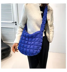 Close-up van gewatteerde blauwe crossbody tas gedragen met een wit vestje aan