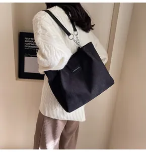 Detalle de un bolso tote grande de pana negra con cadena metálica y etiqueta moda