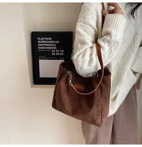 Detalle de bolso tote de pana marrón oscuro con correas de cuero y cadena plateada fina