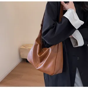 Detail van vintage bruine lederen hobo-tas met textuur en drapering op de schouder van model