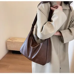 Detail van donkerbruine lederen halfmaanvormige draagtas op model in een beige trenchcoat