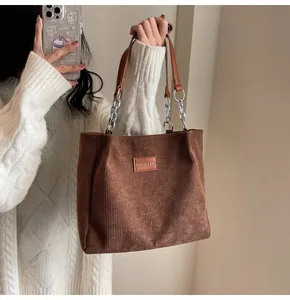 Primer plano de bolso tote de pana marrón con cadena de metal y parche de logo de cuero