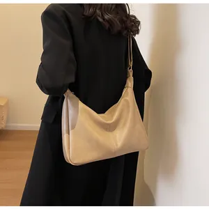Detail van een bruine kunstlederen hobo-tas gedragen door een model in een zwarte wollen jas