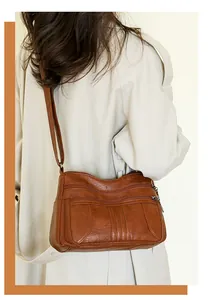 Detail of a brown multi-pocket leather crossbody bag with silver zippers on a model