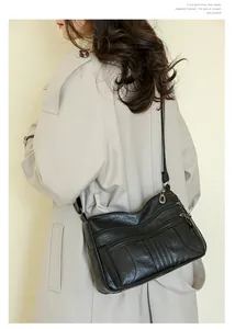 Detail of black multi-zipper leather crossbody bag worn by a model in a beige trench coat