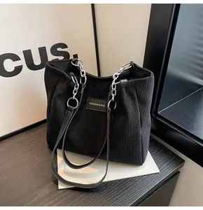 Detalle de bolso tote de pana negra con cadena de metal y etiqueta de cuero de moda