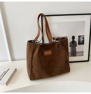 Detalle de bolso tote de pana marrón con rayas verticales y correa de hombro de cuero