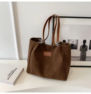 Detalle del bolso tote de pana marrón con etiqueta de logo de cuero y costuras