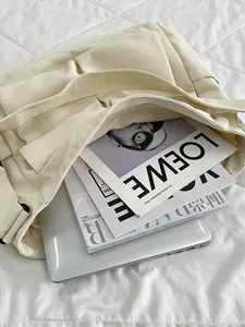 Grande borsa tote in tela crema con tasche frontali su letto bianco con laptop e riviste