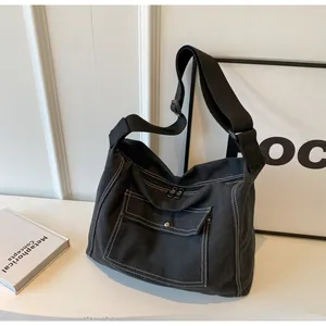 Detalle de bandolera de lona negra con costuras blancas en contraste y bolsillo con solapa