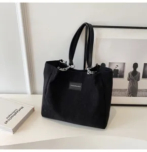 Detalle del bolso tote de pana negra con asas de cuero y parche de logotipo
