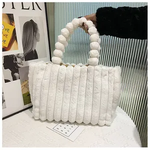 Gros plan du sac cabas en peluche blanche avec matelassage rayé et poignées à pompons