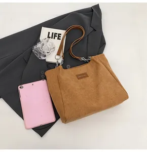 Detalle de un bolso tote de pana marrón con correa de cadena y etiqueta de moda